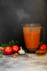 Traditional summer cold tomato soup gazpacho in a blender. Tomatoes, pepper, garlic, basil, parsley, olive oil and croutons. Mediterranean, Spanish cuisine. Front view. Black background. Copy space