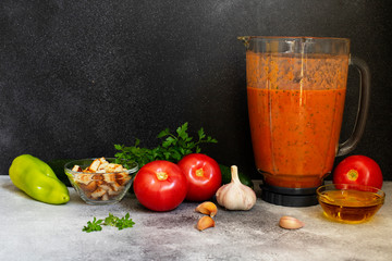 Traditional summer cold tomato soup gazpacho in a blender. Tomatoes, pepper, garlic, basil, parsley, olive oil and croutons. Mediterranean, Spanish cuisine. Front view. Black background. Copy space