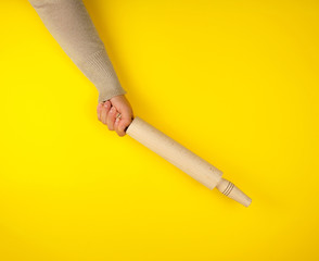 hand holding a wooden rolling pin on a yellow background