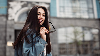 Young beautiful model in the city. Beautiful girl holds sunglasses in hand close-up portrait of a young sexy girl hipster.