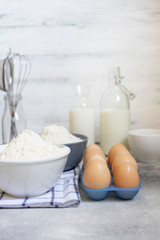 Ingredients for the dough, baking ingredients on a white background. Eggs, milk, flour and wire whisk. Front view. Baking concept. Space for text