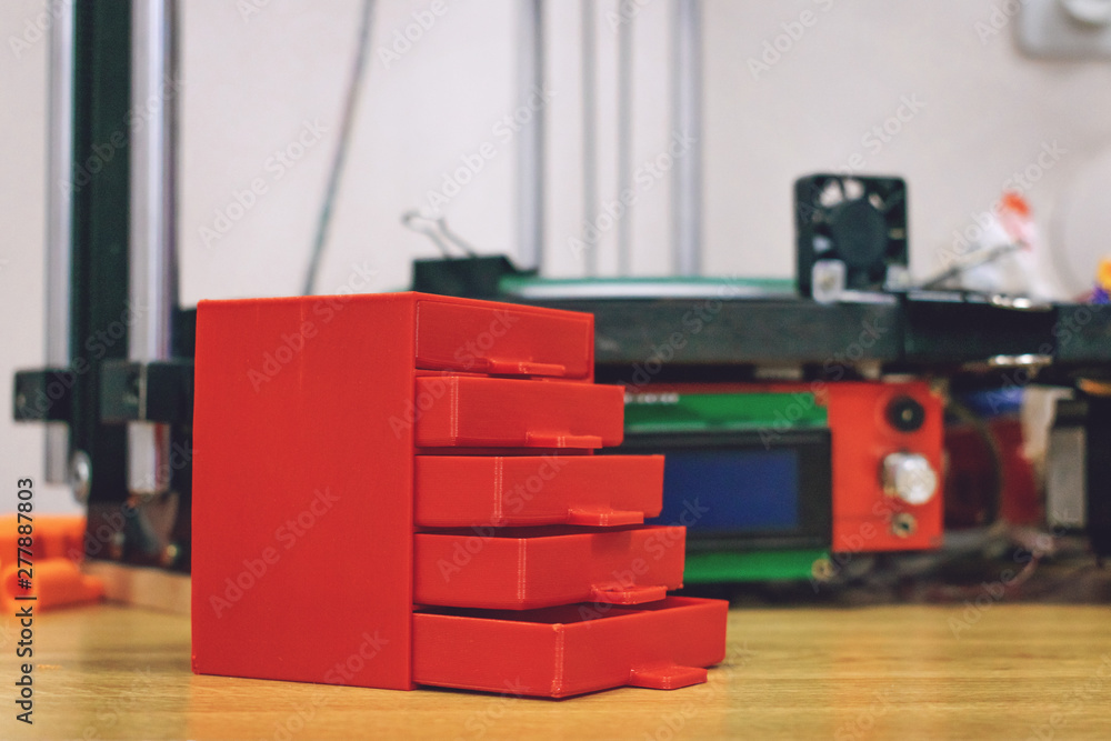 Poster 3d printed red plastic dresser on the background of three dimensional 3d printer. furniture model pr