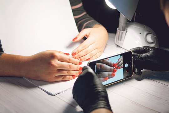 Manicure specialist in black gloves takes pictures of hands with red nails by phone. Manicurist in beauty salon. How shoot nail art design
