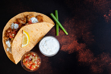 Traditional Mexican fajitas with chicken and vegetables, served in tortilla with white and red sauce, lemon and fresh green onions. Top view. dark background. Copy space