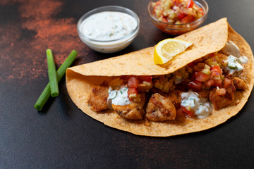 Traditional Mexican fajitas with chicken and vegetables, served in tortilla with white and red sauce, lemon and fresh green onions. Close-up. dark background. Copy space