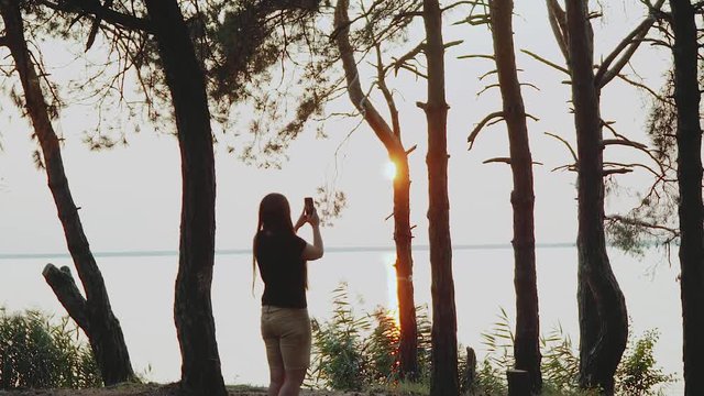 Young woman taking photo with cellphone camera in sunset.Traveller woman taking photo of nature beautiful landscape in background,slow motion.