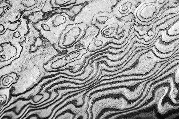 Background with pattern of damask steel. Close up. Macro shot of a damascus knife blade texture. Damascus steel pattern. Metal and steel background. Damascus steel with pattern. Black and white © Aleksei