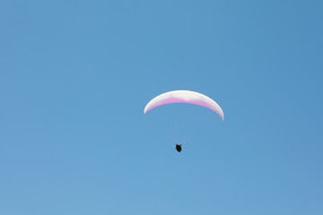 Skydiver with a white-pink parachute flies across the blue sky