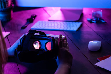 Female hands hold 3d 360 vr headset glasses goggles at work table computer background in futuristic...