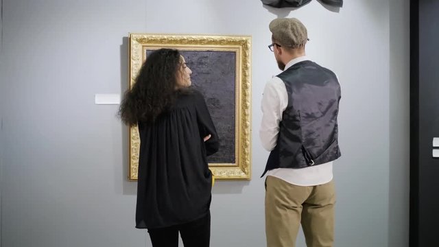 Pair of visitors of exhibit of modern art is chatting in front of pictures