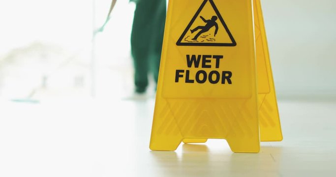 Blurred view of professional cleaner and safety sign "WET FLOOR" indoors
