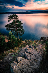 Beautiful sunset landscape on mountain lake with rocks and pine on the foreground