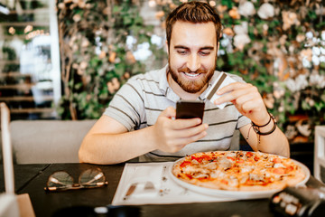 Smiling handsome man paying at restaurant using smartphone and mobile paying technology with credit card