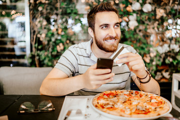 Man paying for pizza using credit card and mobile phone. Modern payment systems concept