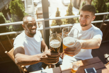 Young group of friends drinking beer, having fun, laughting and celebrating together. Smiling men with beer's glasses in sunny day. Oktoberfest, friendship, togetherness, happiness, summer concept.
