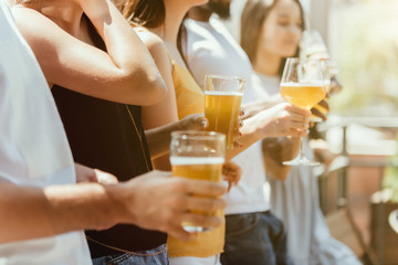 Young group of friends drinking beer, having fun, laughting and celebrating together. Women and men with beer's glasses in sunny day. Oktoberfest, friendship, togetherness, happiness, summer concept.
