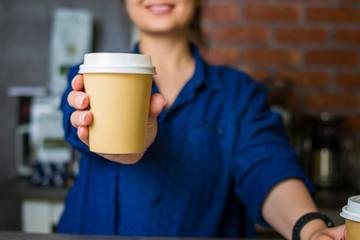 young smiling barista girl holds out her hand with a paper cup of coffee to go