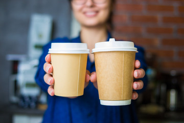 young smiling barista girl holds out her hands with a paper cups of coffee to go