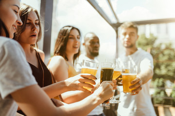 Young group of friends drinking beer, having fun, laughting and celebrating together. Women and men with beer's glasses in sunny day. Oktoberfest, friendship, togetherness, happiness, summer concept.