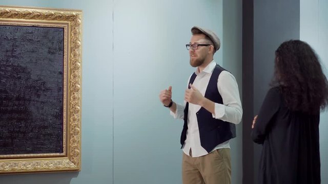 Trendy artist is explaining idea of his picture for female visitor of exhibit