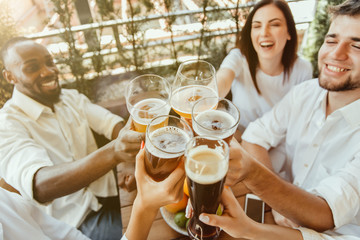 Young group of friends drinking beer, having fun, laughting and celebrating together. Women and men with beer's glasses in sunny day. Oktoberfest, friendship, togetherness, happiness, summer concept.