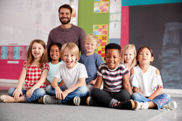Portrait Of Elementary School Pupils Sitting On Floor In Classroom With Male Teacher