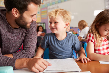 Elementary School Teacher Giving Male Pupil One To One Support In Classroom