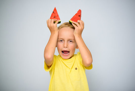 Frolicsome caucasian 5 year old boy child in yellow t-shirt holding two pieces of red watermelon above his head as horns, obstinacy concept.