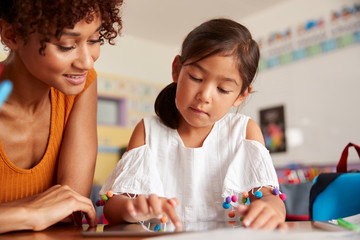 Elementary School Teacher And Female Pupil Drawing Using Digital Tablet In Classroom