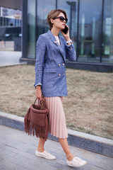 Young stylish Businesswoman is talking by mobile phone outside. Full length Portrait of a Caucasian...