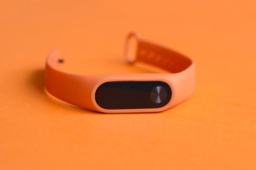 Orange fitness tracker on an orange background close up.
