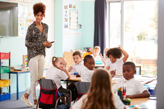 Female Teacher With Digital Tablet Teaches Group Of Uniformed Elementary Pupils In School Classroom