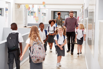 Teacher And Pupils Walking Along Corridor In Busy Elementary School Corridor