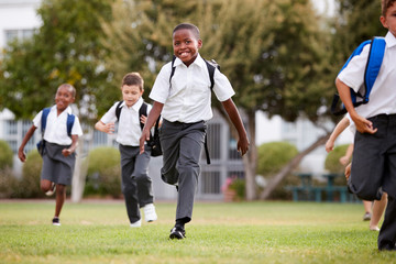 Excited Elementary School Pupils Wearing Uniform Running Across Field At Break Time