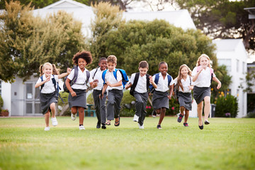 Obraz na płótnie Canvas Excited Elementary School Pupils Wearing Uniform Running Across Field At Break Time