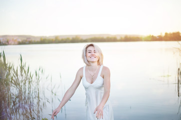 young woman on the beach. The girl in the white dress on the lake enjoys the summer.