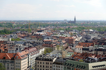 Fototapeta na wymiar Bavarian capital Munich with many buildings roofs and Alps at far bird view in sunny summer day