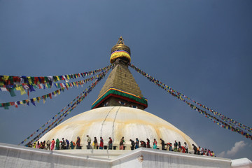 powiewające buddyjskie flagi modlitewne zwisające z kopuły nepalskiej świątyni oraz pielgrzymi