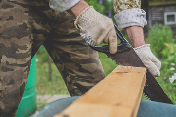 Man in gloves sawing a wooden board with a hand saw