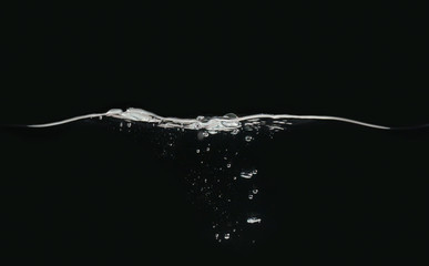 Waving water surface and small bubbles underwater isolated on black background, close up view....