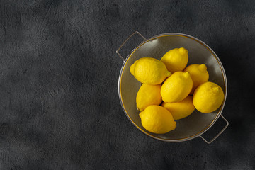 Pile of lemons in colander on a dark background with copy space top view