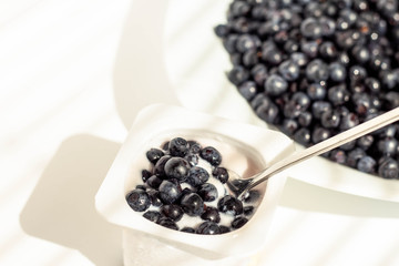 yogurt in the original packaging; fresh blueberries are added to yogurt on top; white background,...