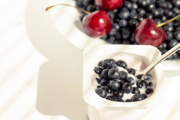 a jar of yogurt in the original packaging; fresh blueberries and sweet cherries are added to yogurt; white background