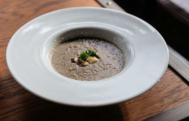 Mushroom soup with Grouton in white plate with sunlight on wooden table.