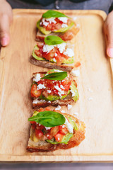 Avocado Toast with Cherry Tomatoes and Feta Cheese, Topping with Rocket leaves. Served on wooden plate.