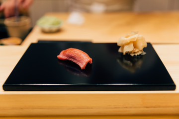 Japanese Omakase meal: Chutoro (Bluefin Tuna) Sushi served by hand with pickled ginger on glossy black plate. Japanese luxury meal.