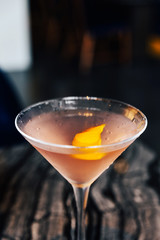 Close-up Pink cocktail filled a sliced of Yuzu peel in wine glass on marble top table.