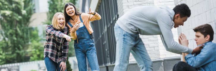 panoramic shot of african american boy in hoodie and jeans bulling boy and teenager shooting it and pointing with fingers