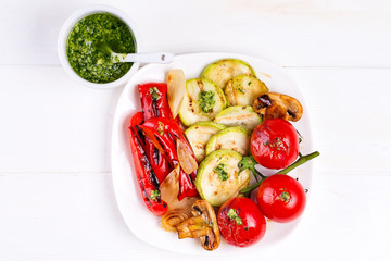 Grilled vegetables on a plate with pesto on white wooden background, flat lay