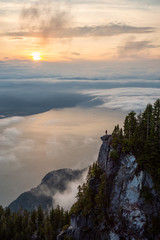 Female Hiker on top of a mountain covered in clouds during a vibrant summer sunset. Taken on top of St Mark's Summit, West Vancouver, British Columbia, Canada.